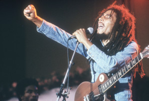 Jamaican Reggae musician, songwriter, and singer Bob Marley performs on stage, in a concert at Grona Lund, Stockholm, Sweden. He extends his fist as he sings into the microphone, with an electric guitar. (Photo by Hulton Archive/Getty Images)