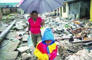 With A boy and a woman walk next to remains of houses destroyed by Hurricane Matthew in Baracoa